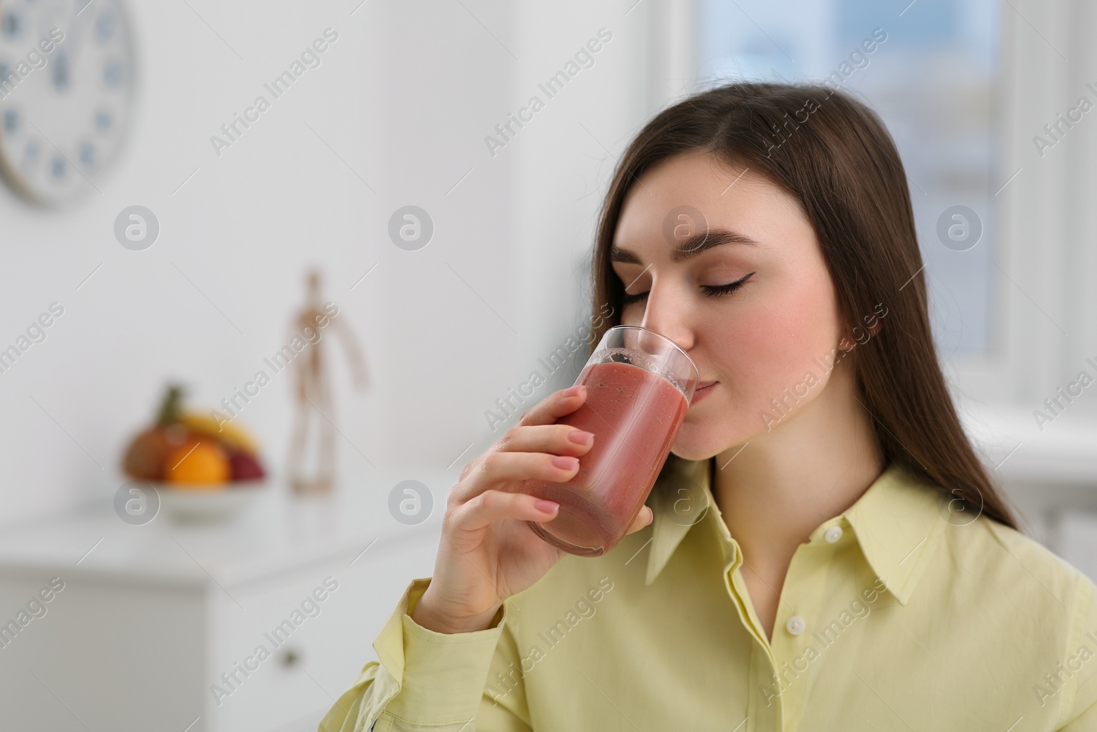 Photo of Beautiful young woman drinking delicious smoothie at home. Space for text