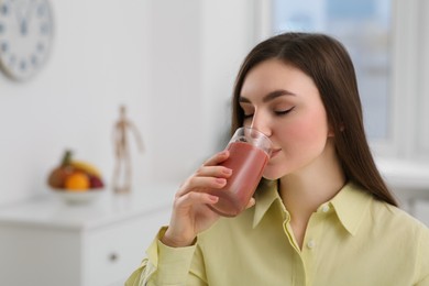 Photo of Beautiful young woman drinking delicious smoothie at home. Space for text