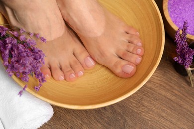 Photo of Woman soaking her feet in bowl with water and lavender, closeup. Pedicure procedure