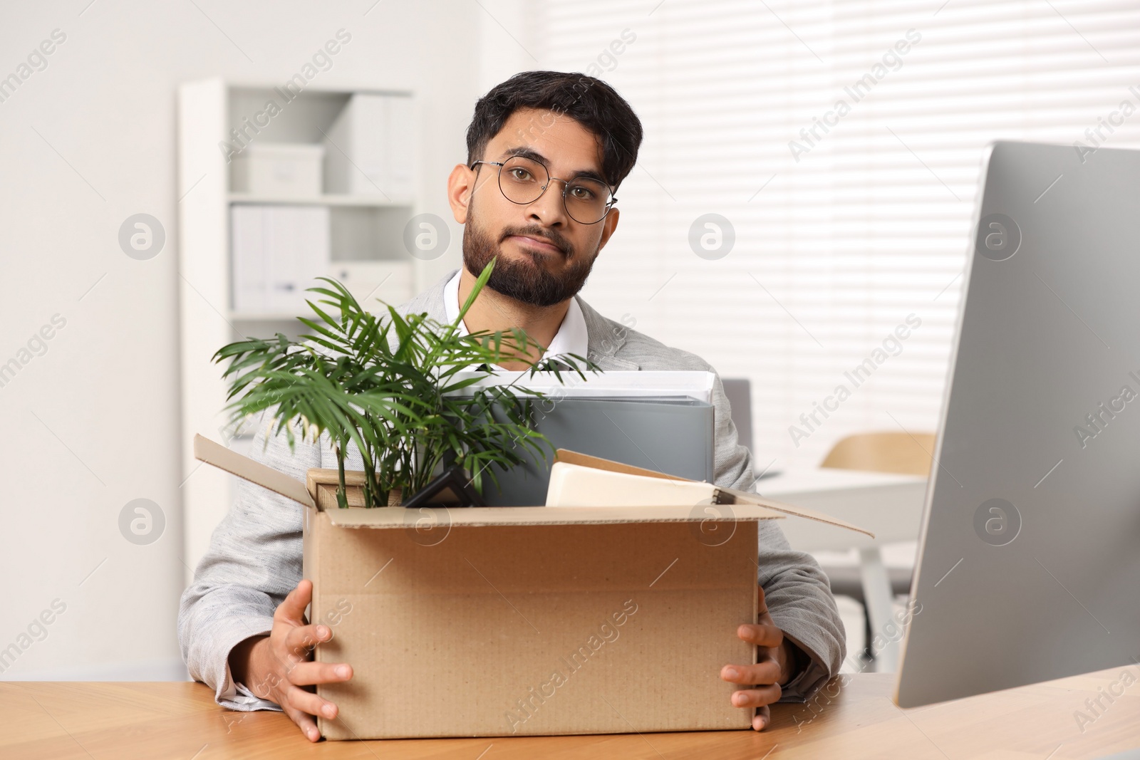 Photo of Unemployment problem. Frustrated man with box of personal belongings at desk in office