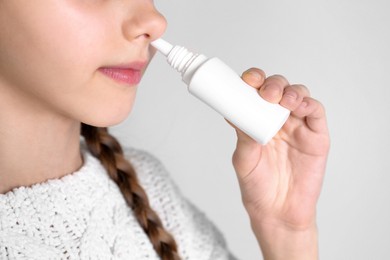 Photo of Sick little girl using nasal spray on white background, closeup