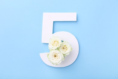 Paper number 5 and beautiful flowers on light blue background, top view