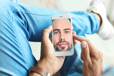 Image of Man using smartphone with facial recognition system indoors, closeup. Biometric verification