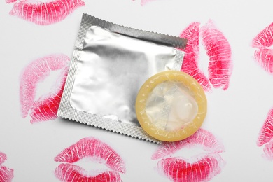 Photo of Condom and lipstick kiss marks on white background, top view. Safe sex