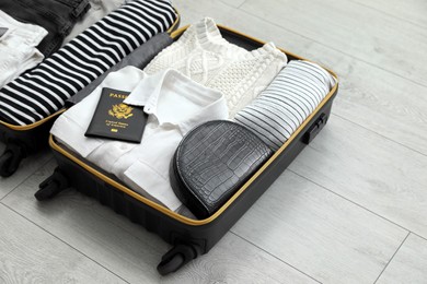 Photo of Open suitcase with clothes, passport and bag on floor