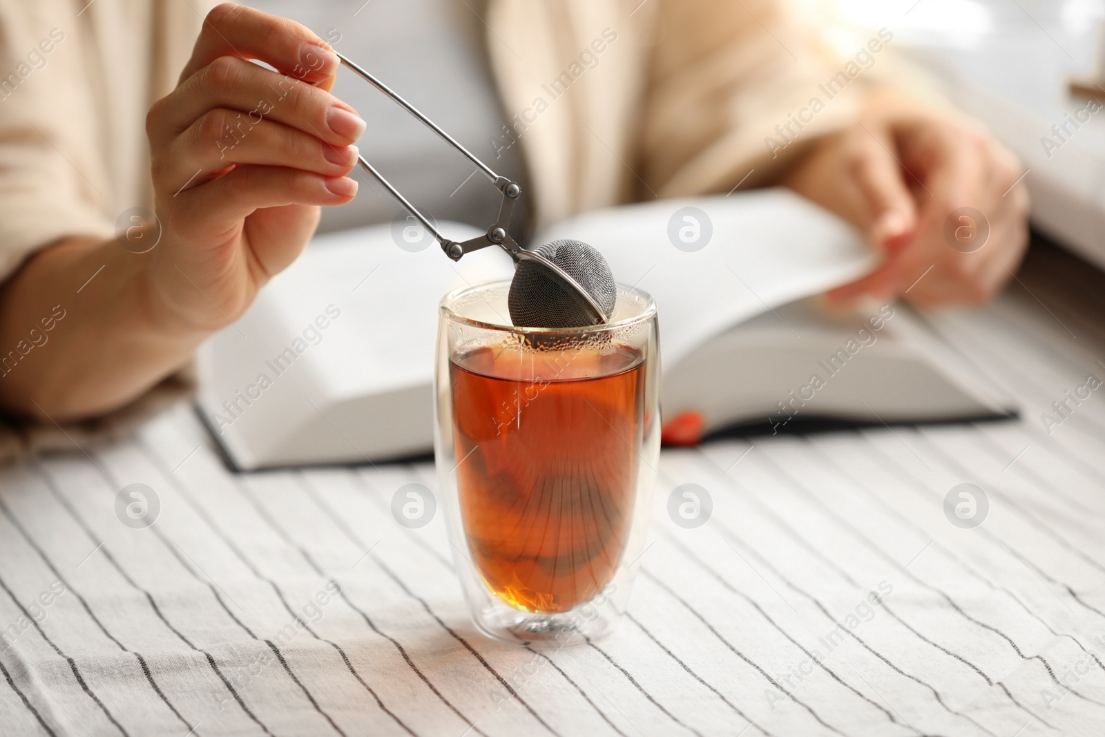 Photo of Woman using snap infuser for brewing tea at table, closeup