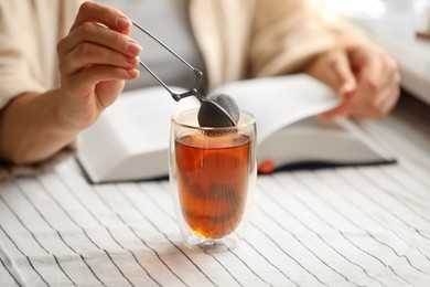 Photo of Woman using snap infuser for brewing tea at table, closeup