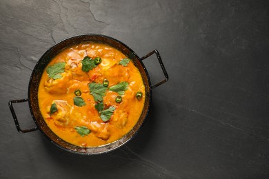 Tasty chicken curry with parsley and pepper on black textured table, top view. Space for text