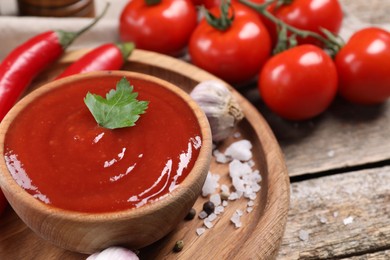 Photo of Delicious ketchup in bowl, chili pepper and spices on wooden table, closeup. Tomato sauce