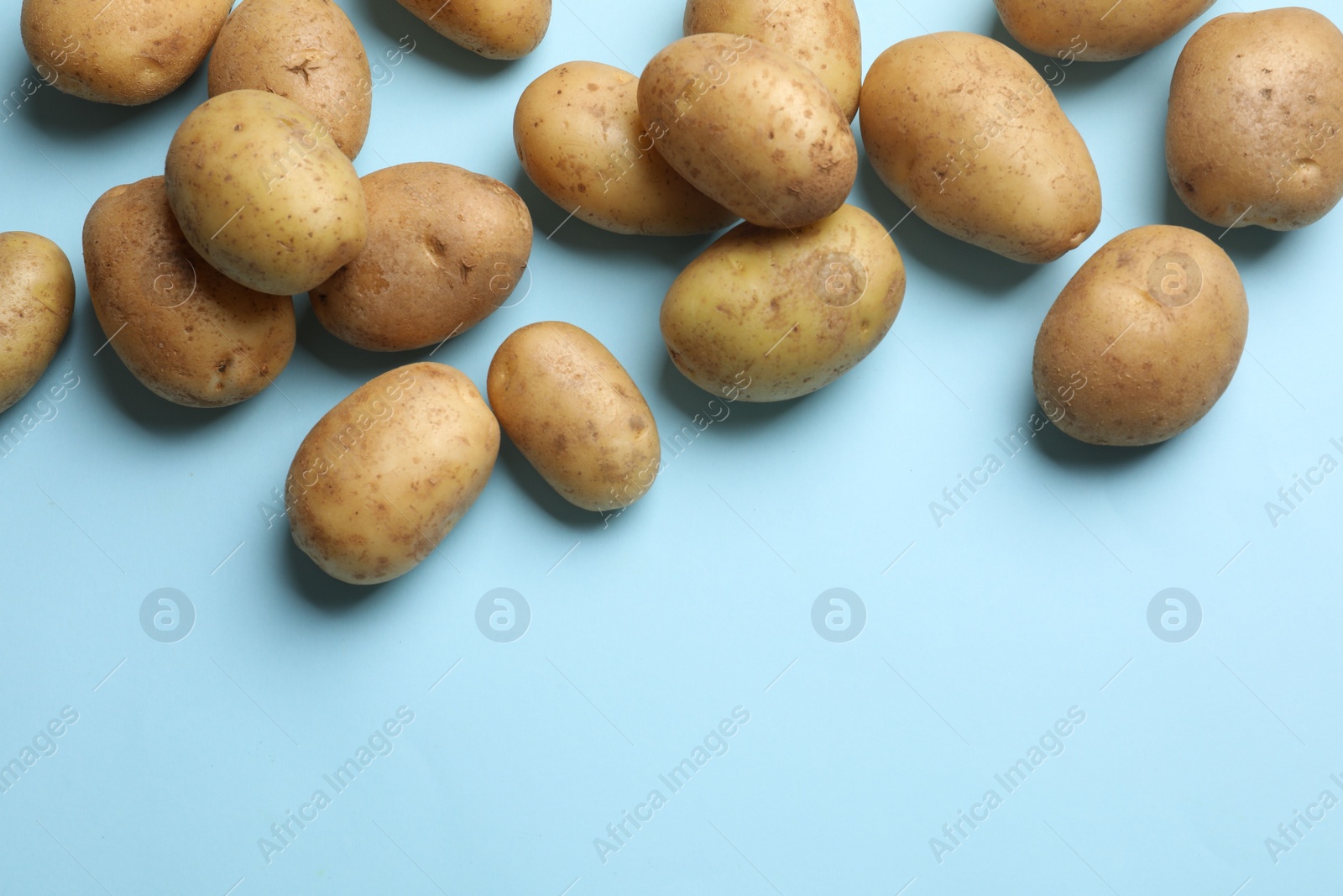 Photo of Many fresh potatoes on light blue background, flat lay. Space for text