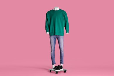 Male mannequin with sneakers dressed in green sweatshirt and jeans on pink background. Stylish outfit