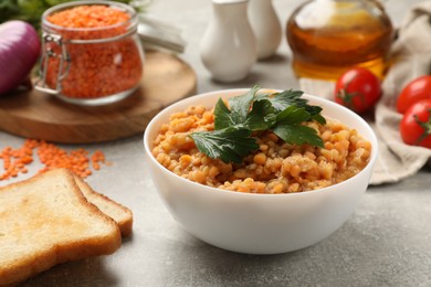 Photo of Delicious red lentils with parsley in bowl served on light grey table, closeup
