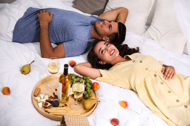 Happy couple with wine and tasty food imitating picnic at home