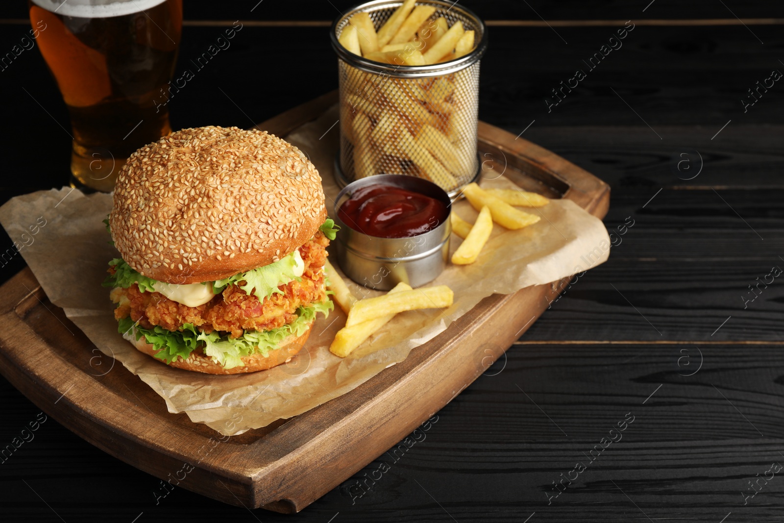 Photo of Delicious burger with crispy chicken patty, french fries, sauce and beer on black wooden table