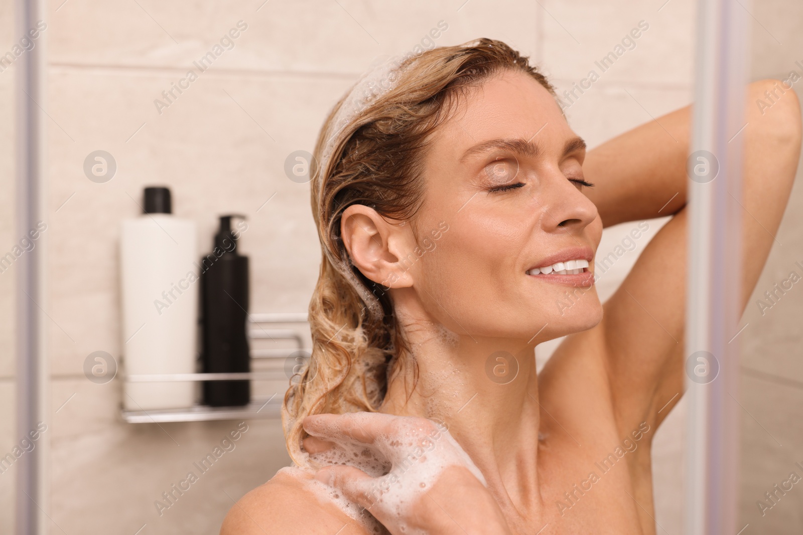 Photo of Beautiful happy woman washing hair in shower. Space for text