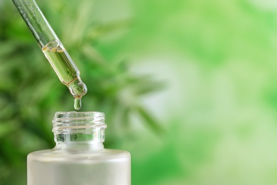 Photo of Dripping of essential oil into bottle on blurred background