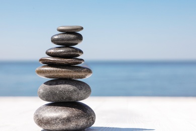 Photo of Stack of stones on wooden pier near sea, space for text. Zen concept