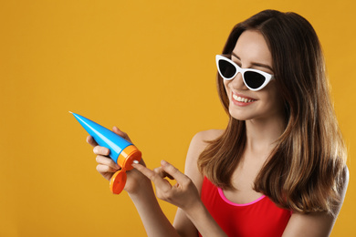 Photo of Young woman applying sun protection cream on orange background