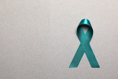 Photo of Teal awareness ribbon on grey paper, top view with space for text. Symbol of social and medical issues
