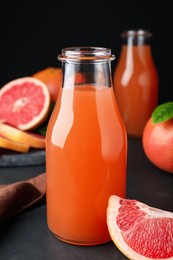 Photo of Tasty freshly made grapefruit juice and fruit on black table