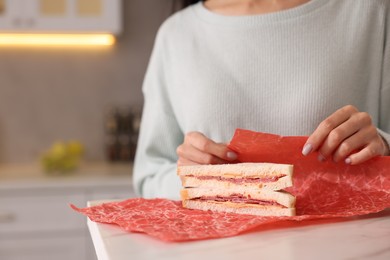 Photo of Woman packing sandwich into beeswax food wrap at light table in kitchen, closeup. Space for text
