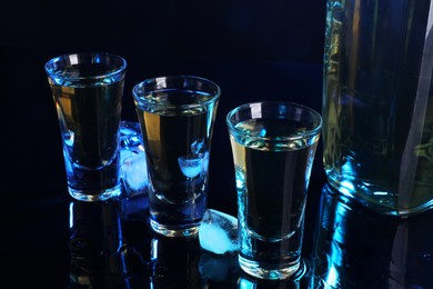 Photo of Alcohol drink in shot glasses, bottle and ice cubes on mirror surface