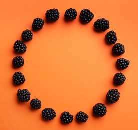 Photo of Frame of ripe blackberries on orange background, flat lay. Space for text