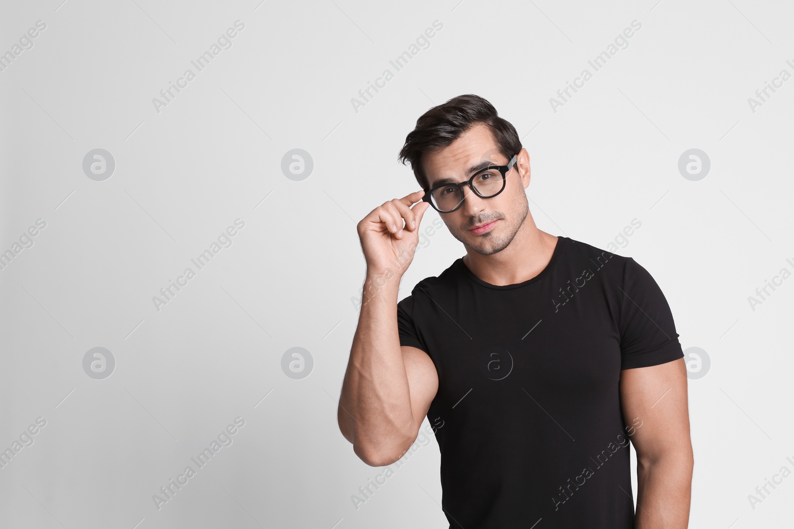 Photo of Portrait of handsome young man in black t-shirt with glasses on grey background. Space for text