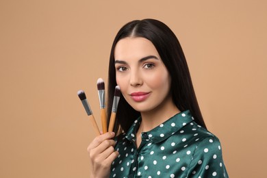 Beautiful woman with different makeup brushes on light brown background. Space for text