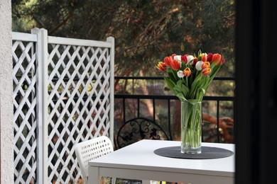 Photo of Beautiful colorful tulips in glass vase on white table at balcony