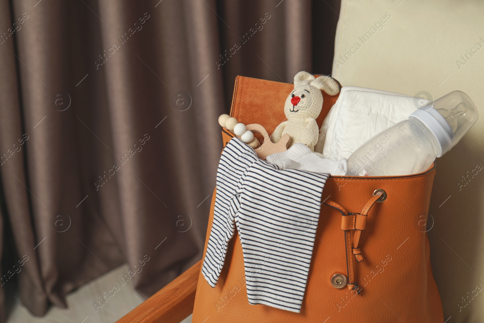 Photo of Mother's bag with baby's stuff on armchair indoors. Space for text