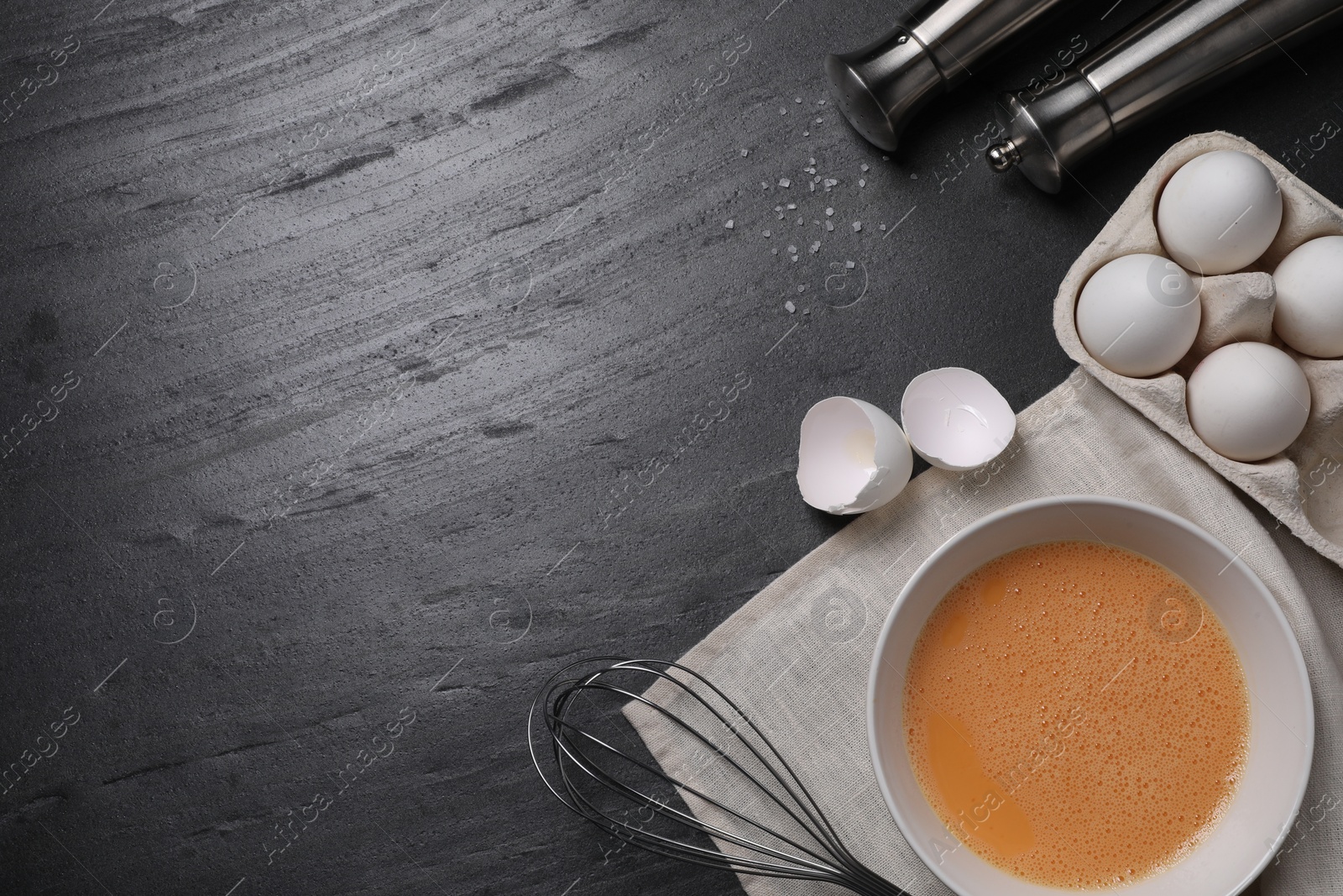 Photo of Metal whisk, beaten eggs and shells on dark grey background, flat lay. Space for text