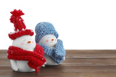 Photo of Cute decorative snowmen in hats and scarves on wooden table against white background, space for text