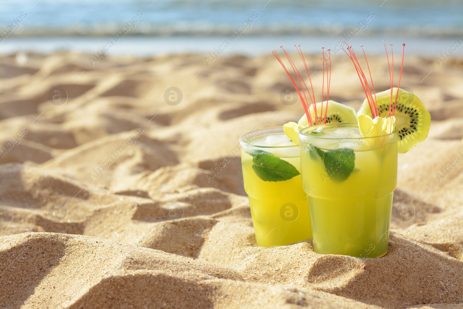 Photo of Glasses of refreshing drink with kiwi and mint on sand near sea. Space for text