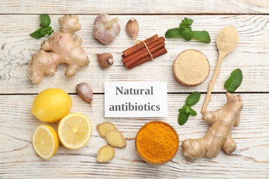 Photo of Different fresh products and card with phrase Natural Antibiotic on light wooden table, flat lay
