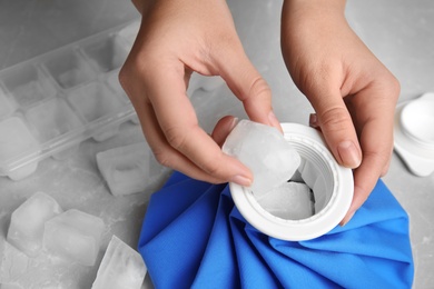 Woman putting ice cubes into pack at marble table, closeup