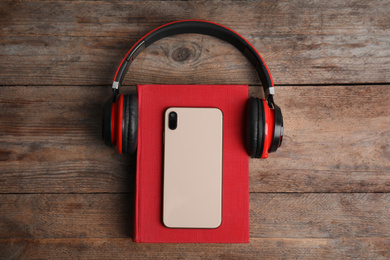 Photo of Book, modern headphones and smartphone on wooden table, top view