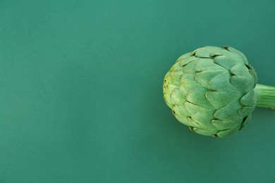 Photo of Whole fresh raw artichoke on green background, top view. Space for text