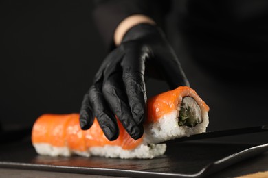 Photo of Chef in gloves making sushi rolls at grey table, closeup