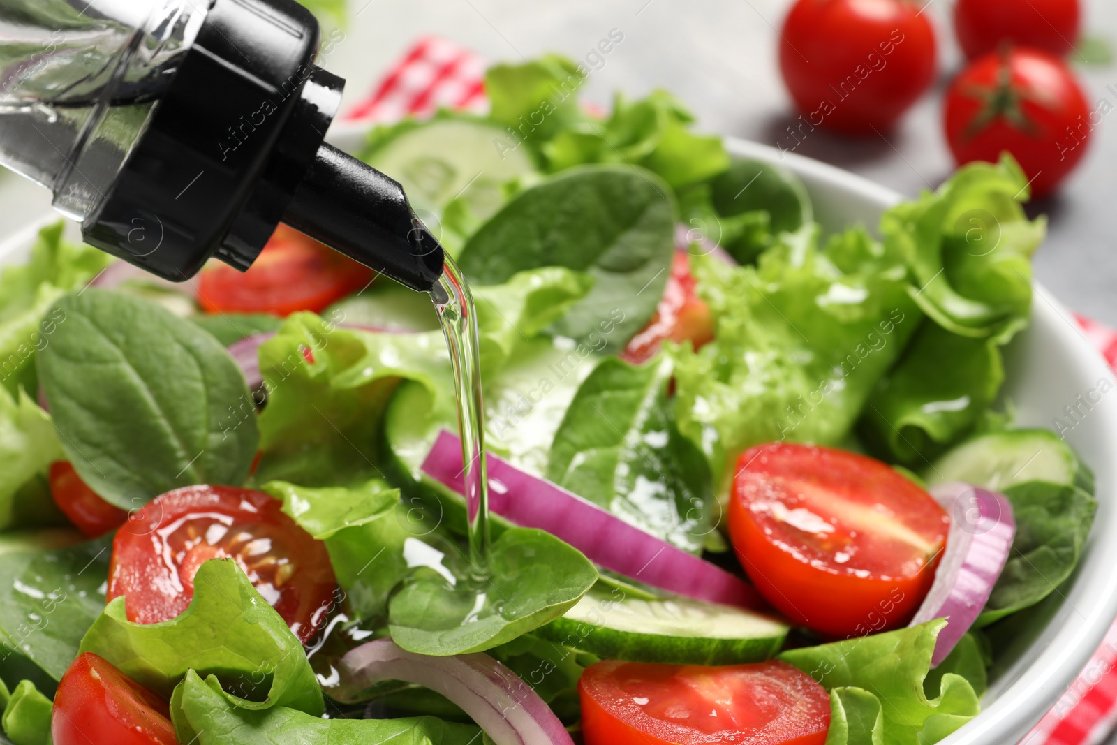 Photo of Pouring oil into delicious vegetable salad in white bowl, closeup