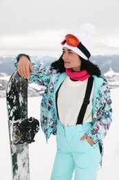 Photo of Beautiful young woman with snowboard on snowy hill. Winter vacation