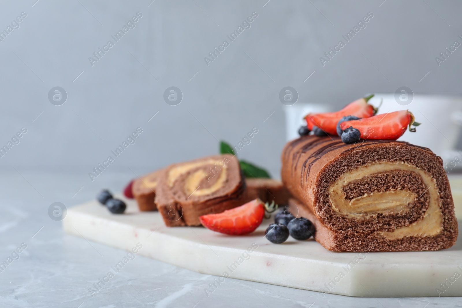 Photo of Tasty chocolate cake roll with cream and berries on light grey marble table. Space for text