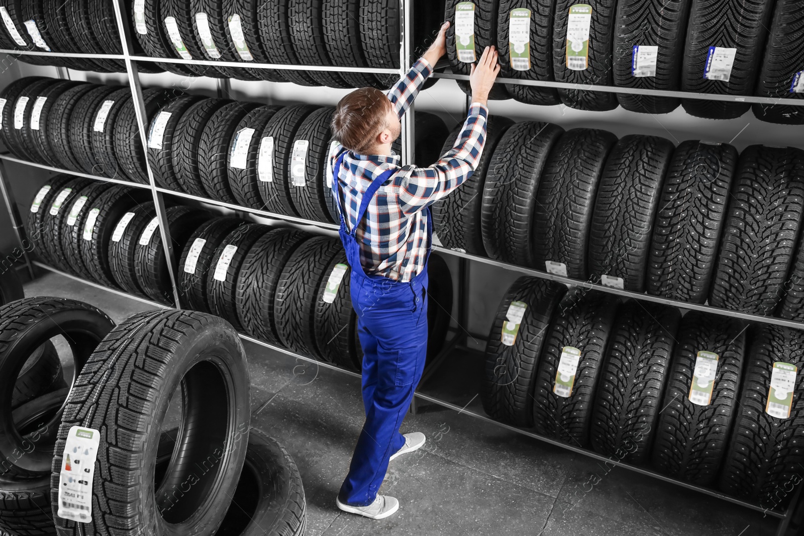 Photo of Young male mechanic with car tires in automobile service center