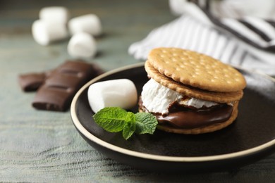 Delicious marshmallow sandwich with crackers, mint and chocolate on light blue wooden table, closeup. Space for text