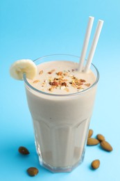 Photo of Glass of tasty banana smoothie with straws and almond on light blue background