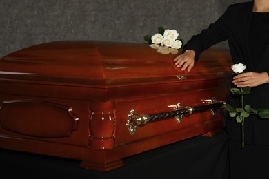 Photo of Young woman with white rose near casket in funeral home, closeup