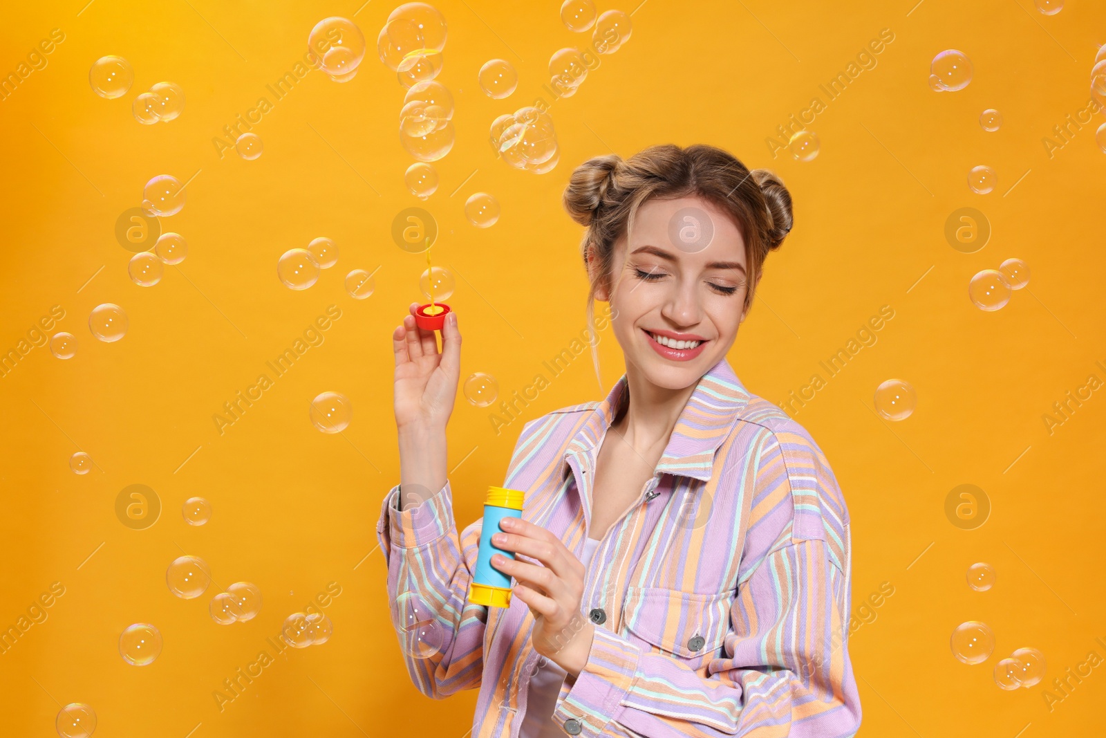 Photo of Young woman blowing soap bubbles on yellow background, space for text