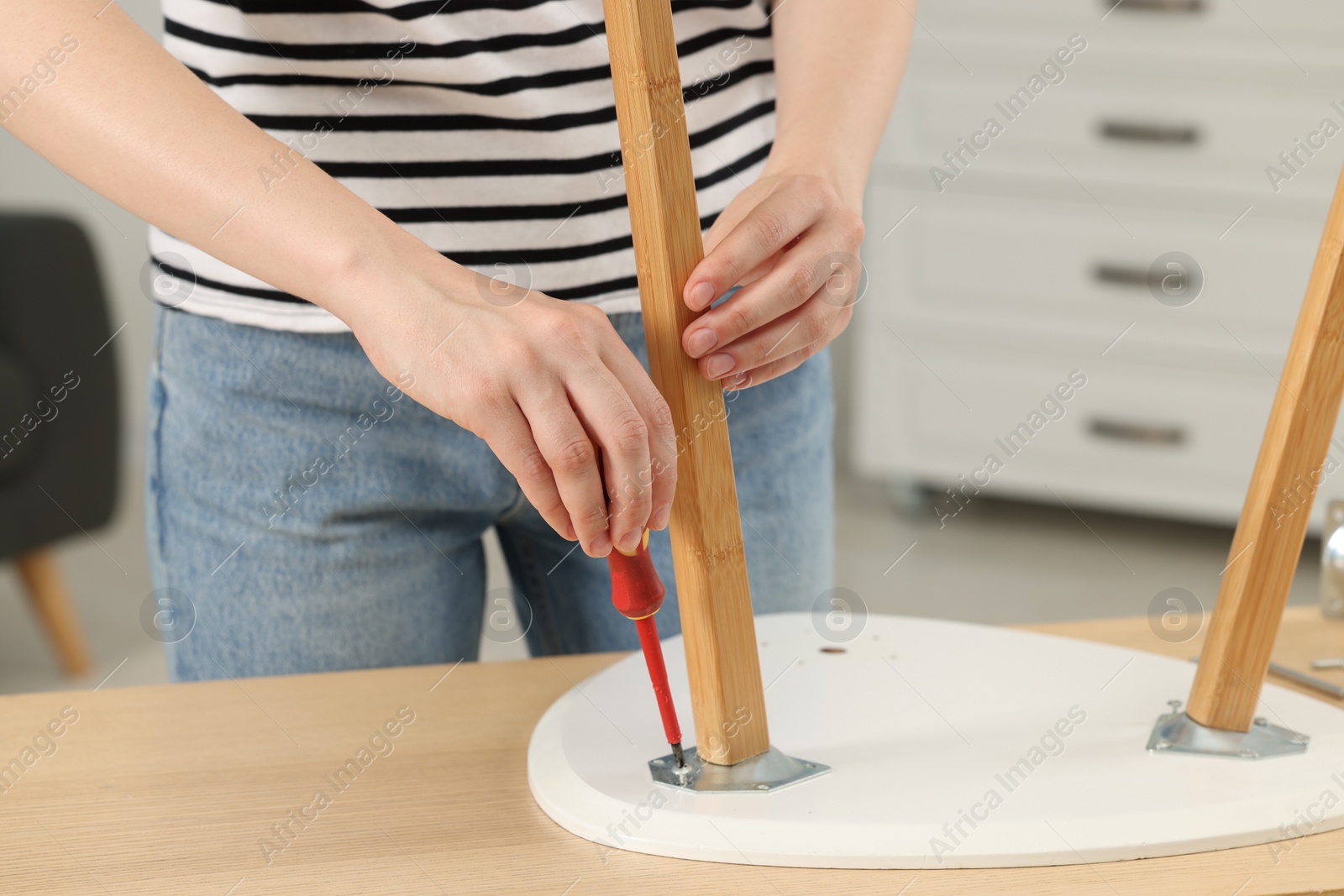 Photo of Woman with screwdriver assembling furniture at table indoors, closeup