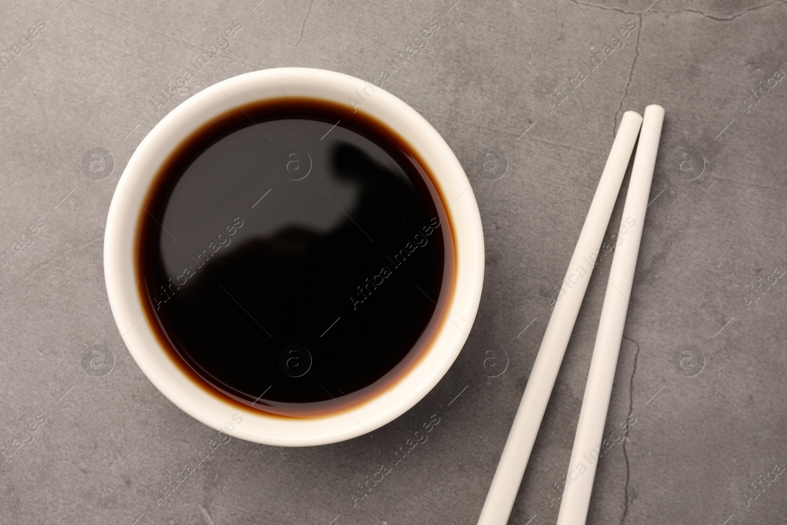 Photo of Bowl of soy sauce and chopsticks on grey table, flat lay