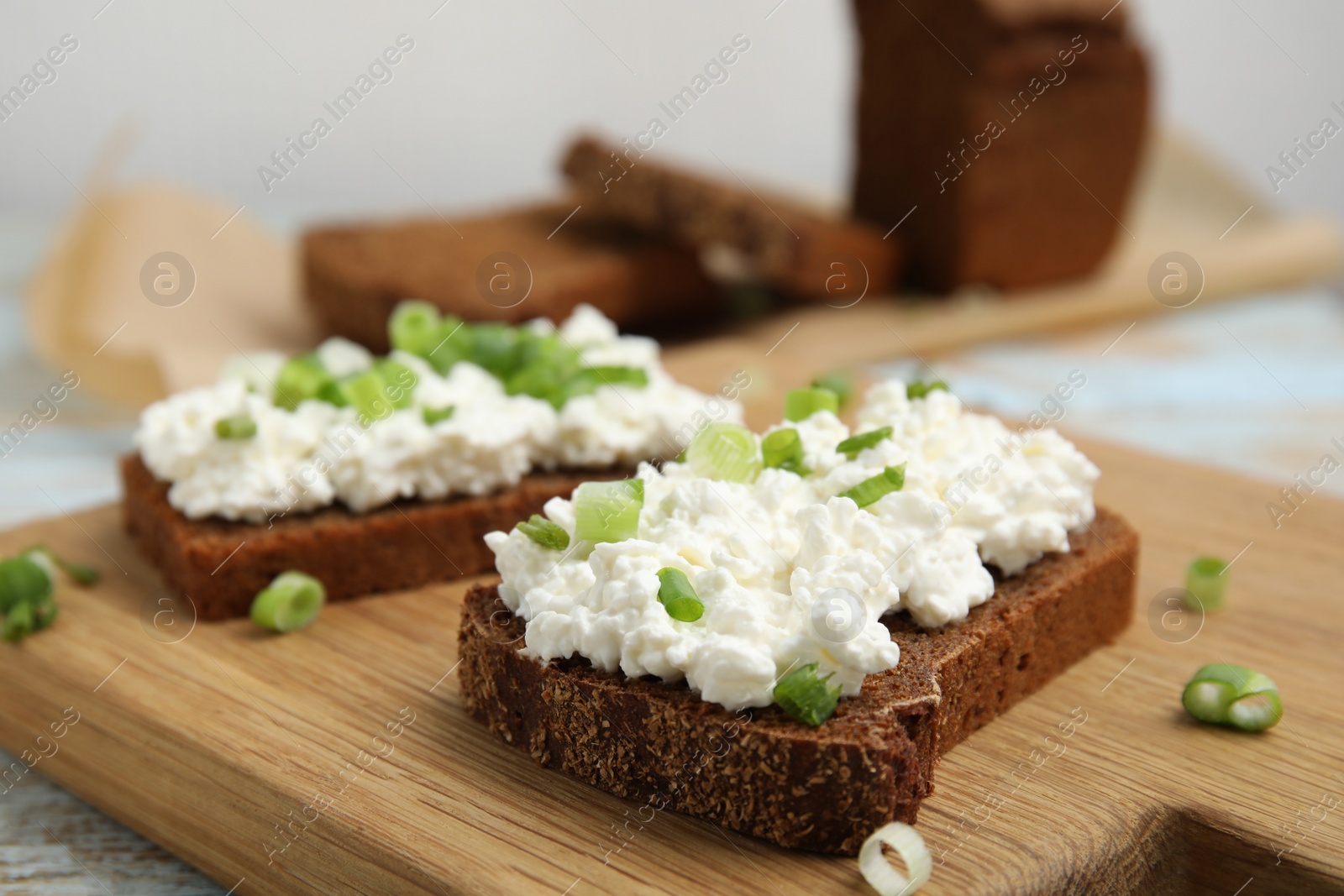 Photo of Bread with cottage cheese and green onion on table, closeup